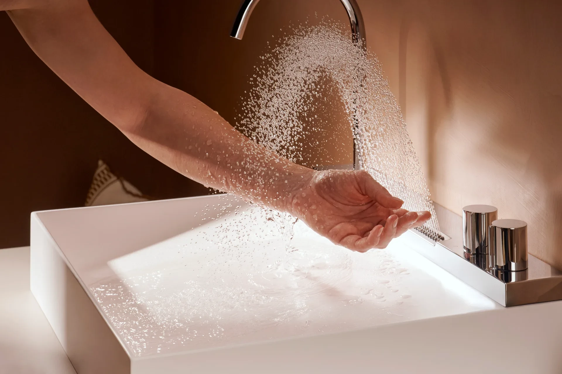 Chorro tipo lluvia de la Avalegra de hansgrohe cayendo sobre una mano abierta, sobre la cubeta blanca de SolidSurface