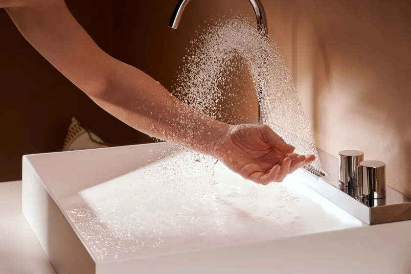 Chorro tipo lluvia de la Avalegra de hansgrohe cayendo sobre una mano abierta, sobre la cubeta blanca de SolidSurface
