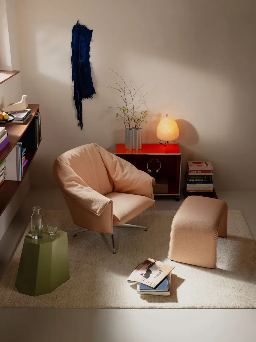 Butaca Bascule de Vitra tapizada en tela rosa arena, con base giratoria de aluminio y otomana a juego, en un rincón de lectura junto a una librería y una lámpara de papel
