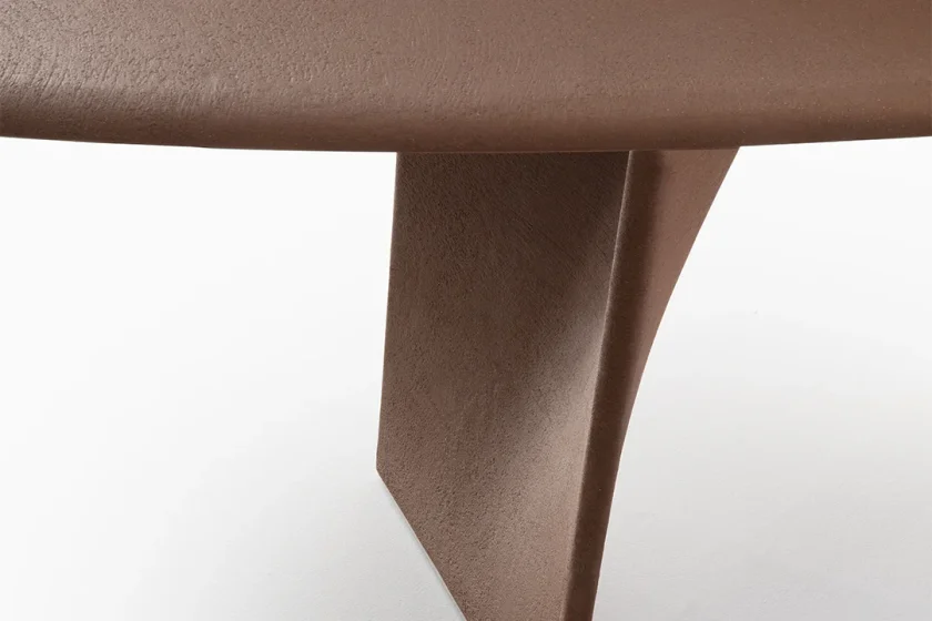 Detalle del canto de un sobre de mesa Rimadesio y su pata en forma de aleta, acabados en Terrae, un mineral mate de tono tierra, sobre fondo blanco